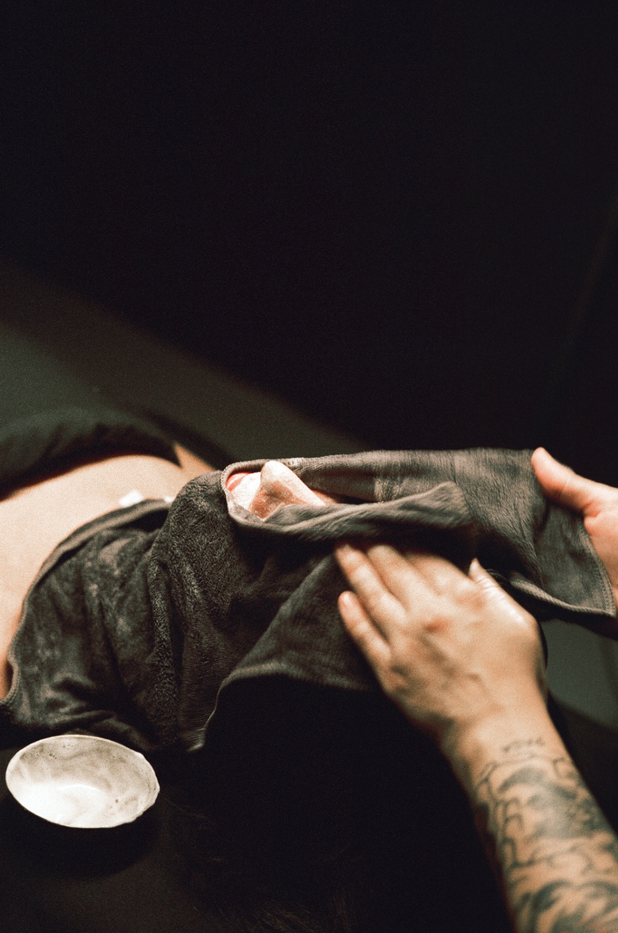 Warm towel being unfolded over a client's face at the end of a treatment